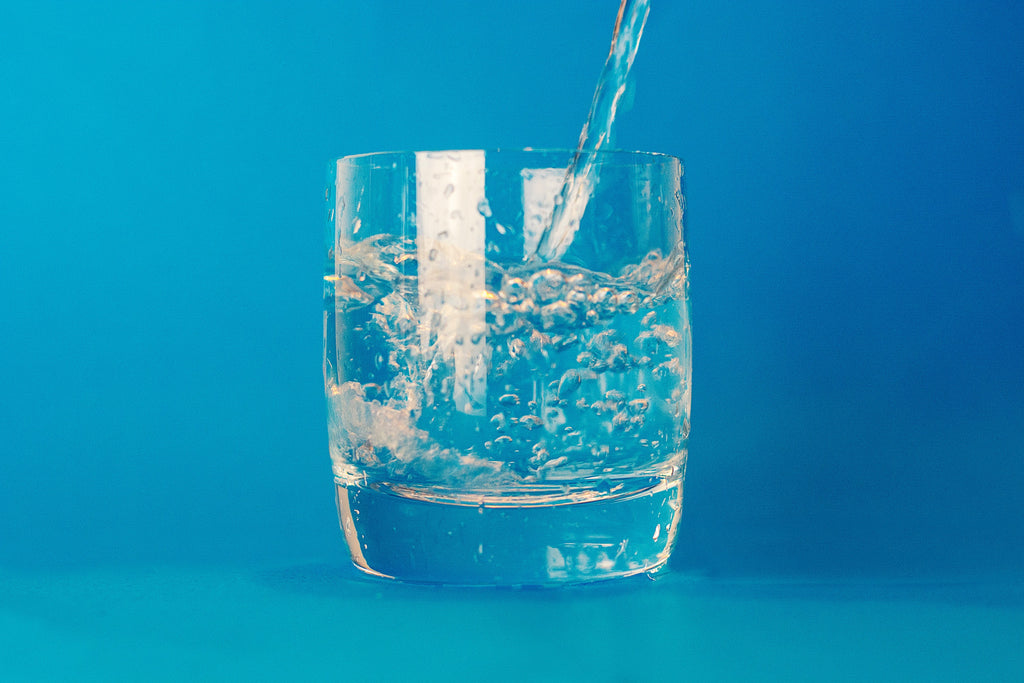 water pouring into drinking glass on blue background