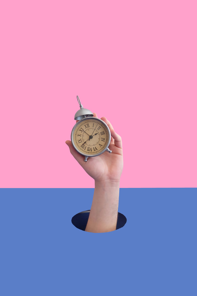 hand popping up from hole holding alarm clock against pink and blue background