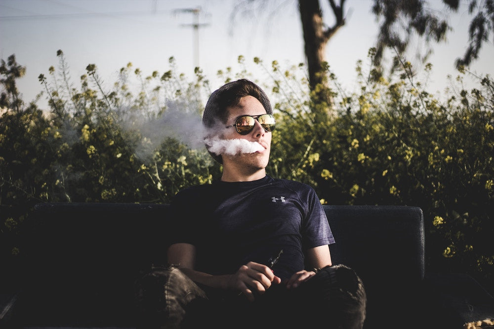 Man exhaling ecigarette in front of flowers