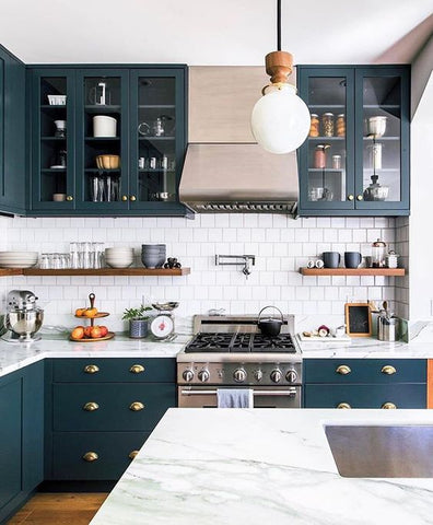 A view of a sustainable kitchen with navy cabinets, white countertops, and brass light fixtures 