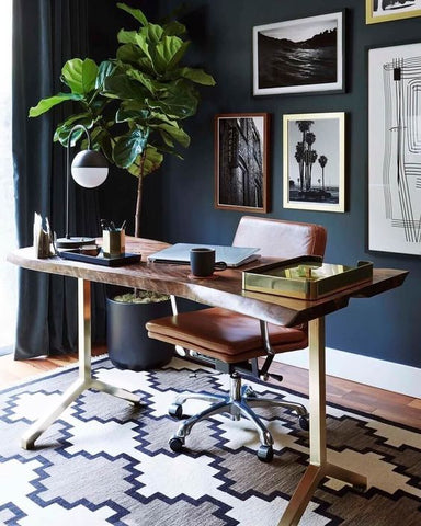 A minimal office with navy walls and a wooden desk with a laptop on it 