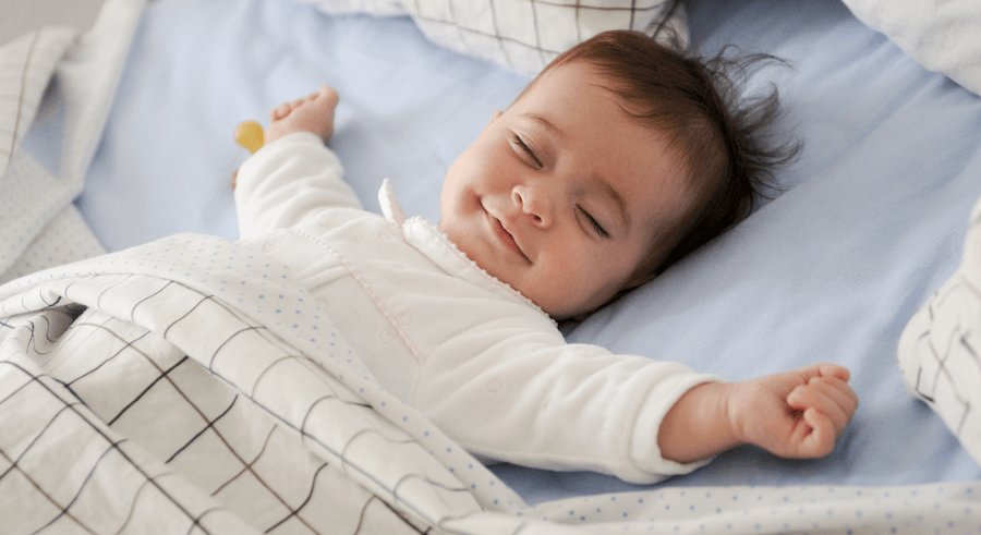 happy baby sleeping peacefully on bed with arms out