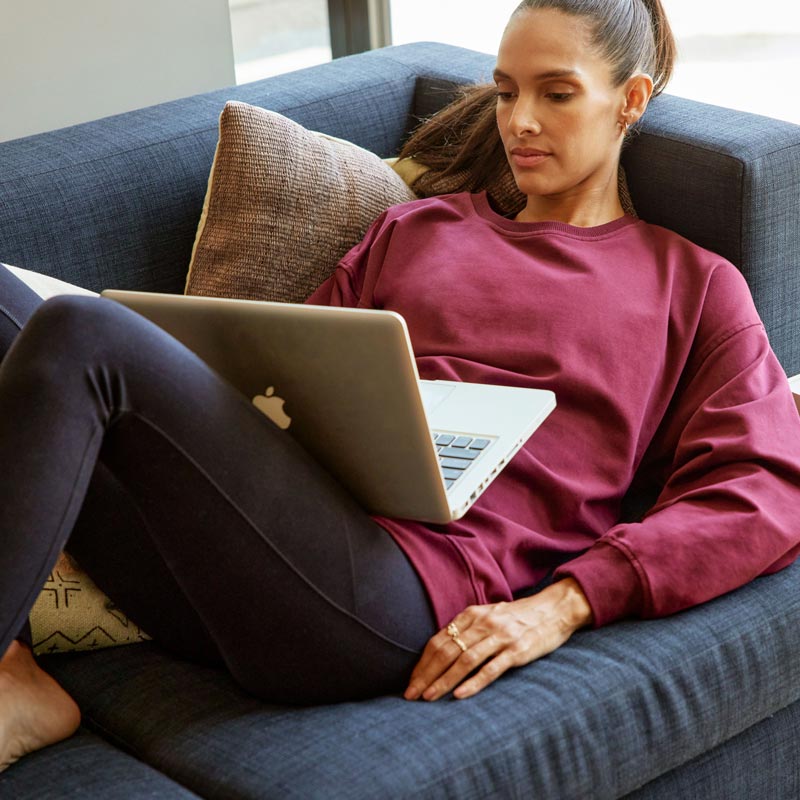 MPG female model lounging on a couch checking in with friends on her laptop