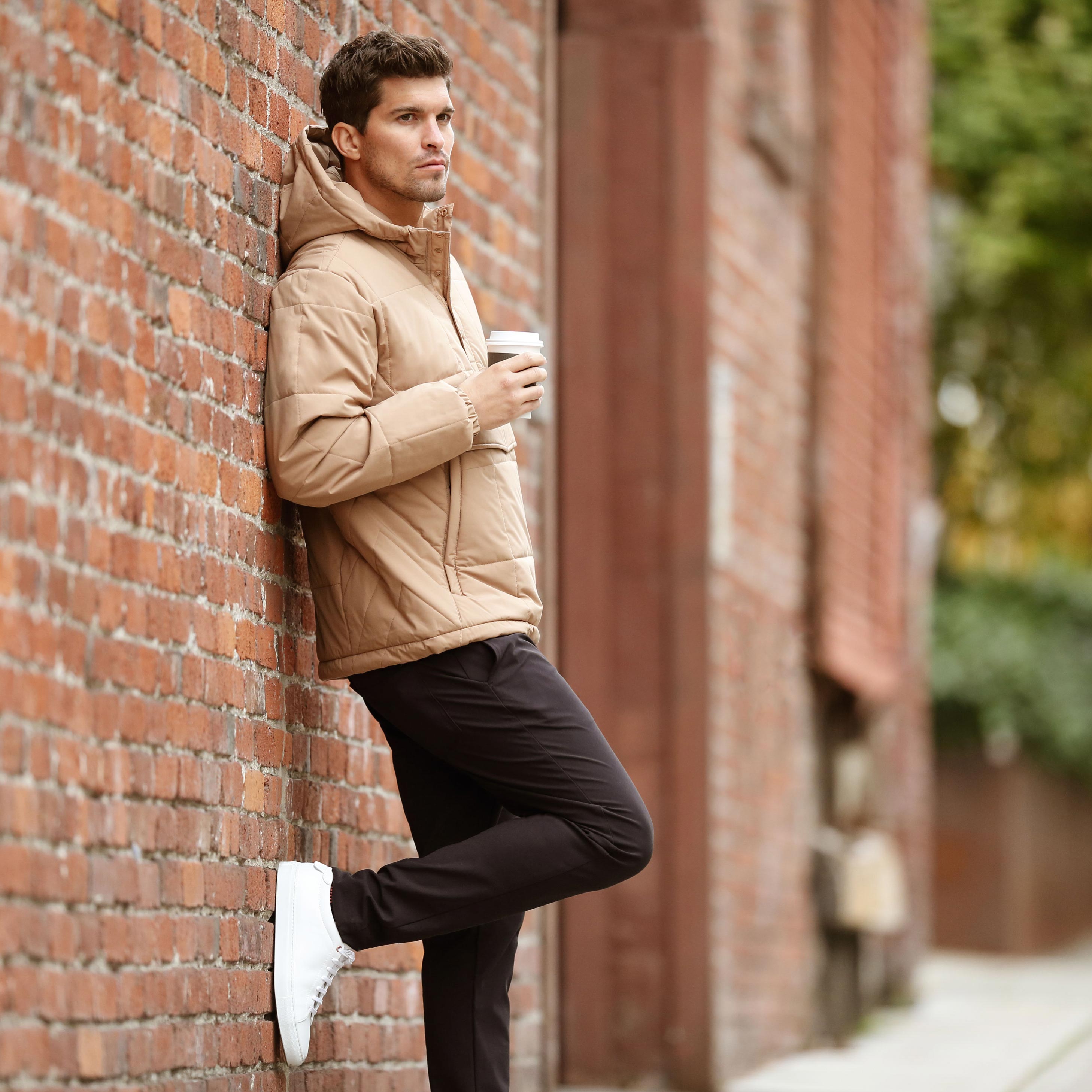 MPG male model leaning on a brick wall outside enjoying a coffee