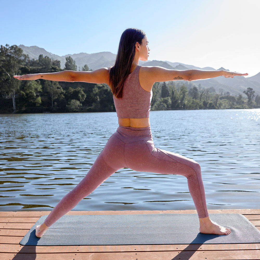MPG female model on a dock in front of a beautiful lake doing a yoga pose, wearing pink MPG activewear