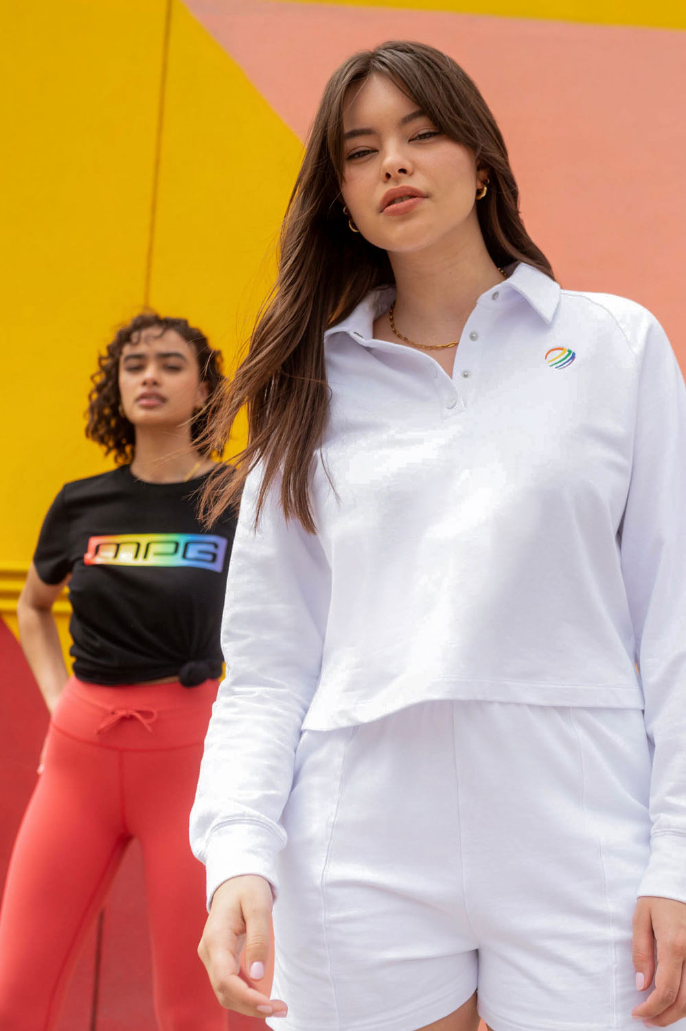 Two gay females posing in MPG Pride collection t-shirts, one girl is in the background