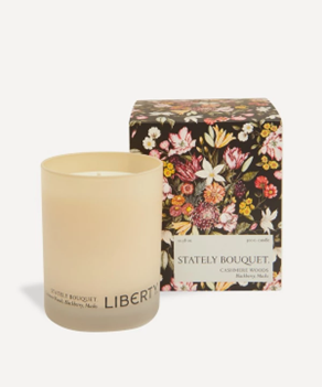 A scented candle in a beige glass vessel positioned next to vibrant floral packaging from <span data-mce-fragment="1"><a href="https://www.libertylondon.com/uk/stately-bouquet-scented-candle-300g-R459511006.html?utm_term=459511006&amp;gad_source=1&amp;gclid=Cj0KCQiAwP6sBhDAARIsAPfK_wZUhACUnmKcktFGrdOnFQRjcXGpnejd5I5wSlOw6JN3PeBHaBIYQ5QaAo5oEALw_wcB" data-mce-fragment="1" data-mce-href="https://www.libertylondon.com/uk/stately-bouquet-scented-candle-300g-R459511006.html?utm_term=459511006&amp;gad_source=1&amp;gclid=Cj0KCQiAwP6sBhDAARIsAPfK_wZUhACUnmKcktFGrdOnFQRjcXGpnejd5I5wSlOw6JN3PeBHaBIYQ5QaAo5oEALw_wcB">LIBERTY</a></span>.