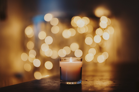 A lit candle in focus in front of some ambient lights that are out of focus in the shot. Source: <span data-mce-fragment="1"><a href="https://pixabay.com/photos/candle-flame-bokeh-burning-candle-5859094/" data-mce-fragment="1" data-mce-href="https://pixabay.com/photos/candle-flame-bokeh-burning-candle-5859094/">Pixabay</a></span>.