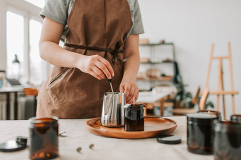 A person placing a thermometer in a pot of melted wax, about to pour it in a homemade candle. Sourced from <span data-mce-fragment="1"><a href="https://www.pexels.com/photo/person-wearing-an-apron-holding-a-stainless-pitcher-6755808/" data-mce-fragment="1" data-mce-href="https://www.pexels.com/photo/person-wearing-an-apron-holding-a-stainless-pitcher-6755808/">Pexels</a></span>