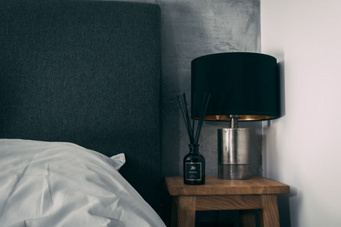 A product image of a black reed diffuser positioned on a bedside table. Source: <span data-mce-fragment="1"><a href="https://unsplash.com/photos/stainless-steel-cup-on-brown-wooden-table-NqbHuzCNBv0" data-mce-href="https://unsplash.com/photos/stainless-steel-cup-on-brown-wooden-table-NqbHuzCNBv0" data-mce-fragment="1">Unsplash</a></span>.