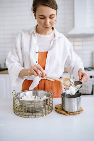 A woman using a double-boiler to melt candle wax. Sourced from <span data-mce-fragment="1"><a href="https://www.pexels.com/photo/woman-puts-candle-wax-into-stewpan-7234502/" data-mce-fragment="1" data-mce-href="https://www.pexels.com/photo/woman-puts-candle-wax-into-stewpan-7234502/">Pexels</a></span>.