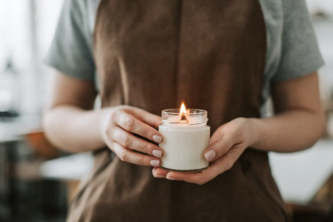 <span style="font-weight: 400;">A person holding a lit candle in a glass jar. Sourced from </span><a href="https://www.pexels.com/photo/person-in-brown-apron-holding-candle-6755862/"><span style="font-weight: 400;">Pexels</span></a><span style="font-weight: 400;">.</span>