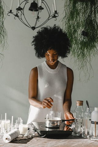 <span style="font-weight: 400;">A woman heating up soy wax using the double boiler method. Sourced from </span><a href="https://www.pexels.com/photo/tranquil-black-woman-making-candles-on-cooker-in-workshop-5761131/"><span style="font-weight: 400;">Pexels</span></a><span style="font-weight: 400;">.</span>