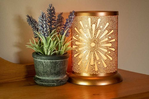 A golden electric wax melt warmer positioned on a shelf. Image sourced from Owlchemy.