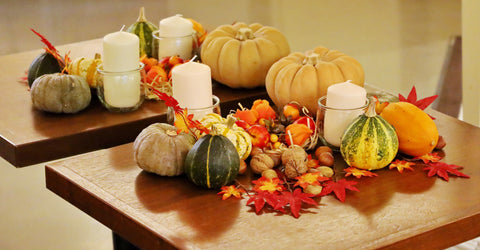 Pillar candles in glass vessels positioned among mini pumpkins in different colours.