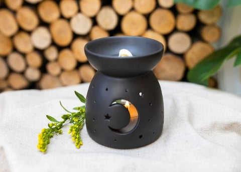 A black tealight wax melt burner with a burning wax melt on top. Image sourced from Blooms & Candy Flower Studio.