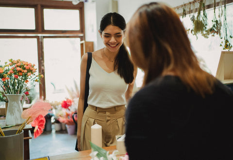 A smiling woman standing at the till while a shop assistant serves her. Sourced from Pexels.