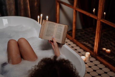 A woman reading in a bubble bath in a room lit up by candles. Sourced from Pexels.