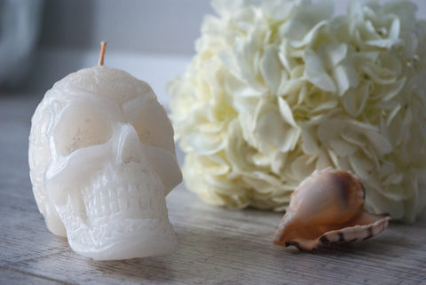 A white skull-shaped candle positioned next to flowers and a shell.