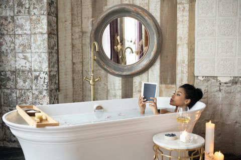 A woman reading a book in a bath with pillar candles at the side.