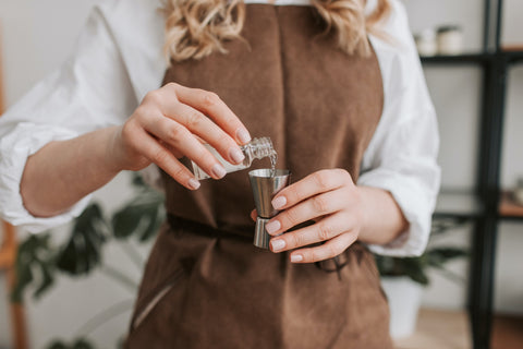 Woman pouring candle-making fragrance oils into a measure.
