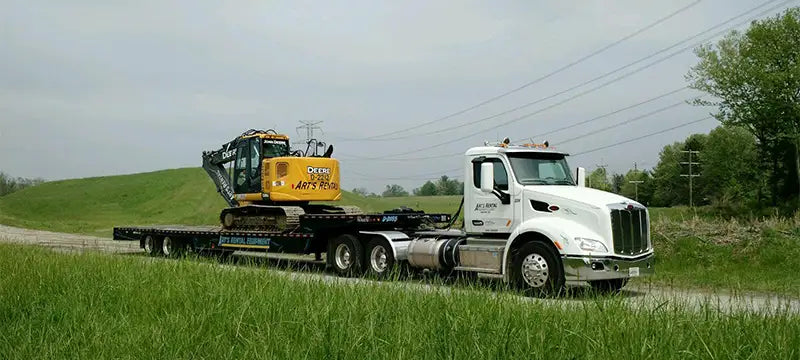 Semi truck hauling an excavator on a dirt road