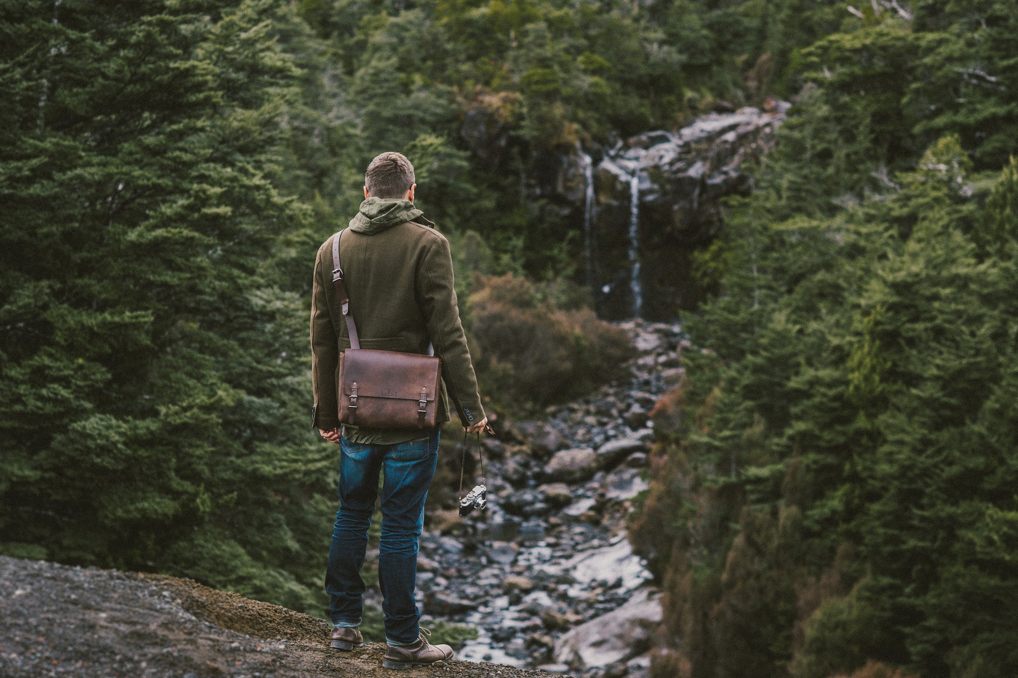 A man standing looking at a waterfall with his Loyal Workshop Bag over his Shoulder.