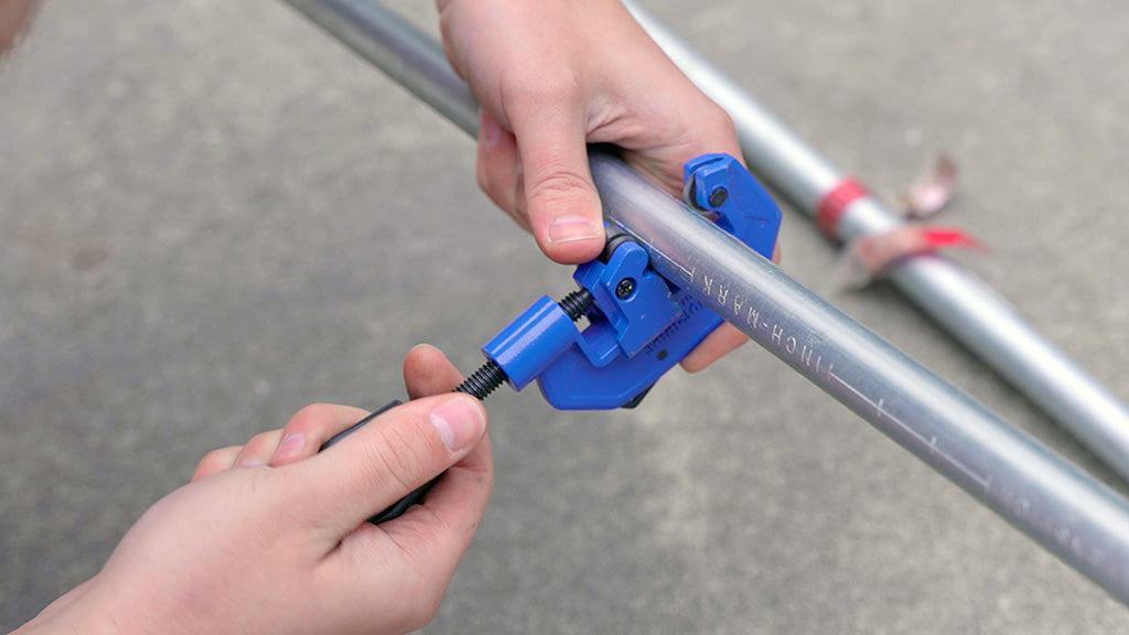 hands holding a pipe cutter and using it on a piece of conduit