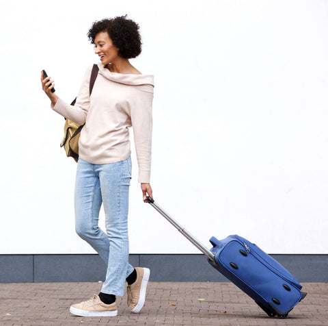 woman pulling a suitcase while looking into her phone