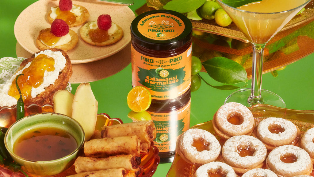 A jar of Pika Pika calamansi marmalade on a table filled with cookies, lumpia, calamansi fruit and a cocktail.