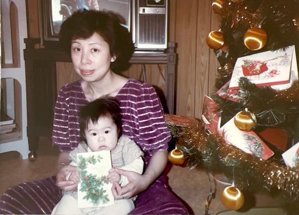 A childhood photo of Kat Lieu, the founder of the Subtle Asian Baking community and cookbook author of Modern Asian Baking At Home, with their mother in front of a Christmas tree.