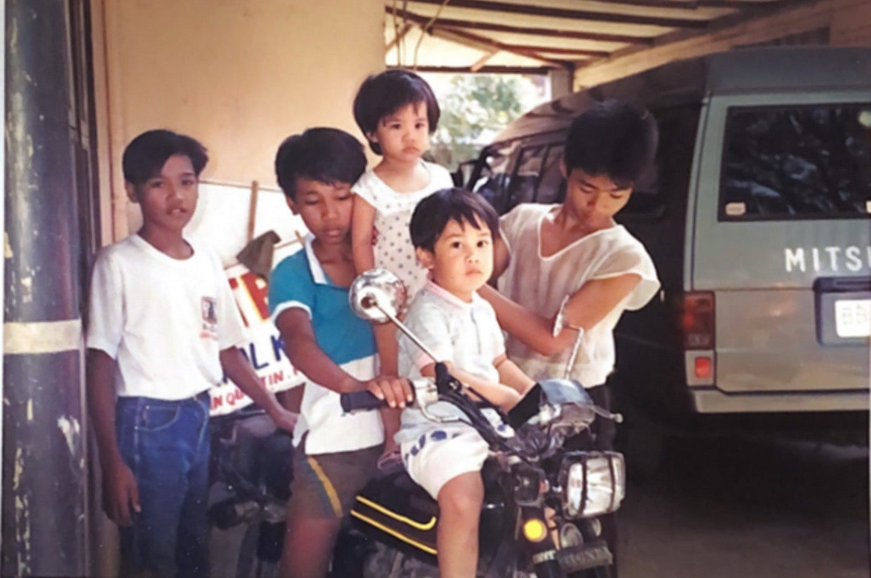 A childhood photo of Victoria and Miggy Reyes, the sibling co-founders of Narra, sitting on a motorbike with other children.