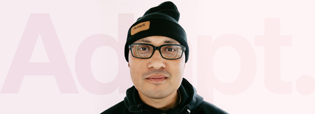 A headshot of Evan Lessler, the CEO of Adapt Clothing, with a faded Adapt logo on a pink background behind him.