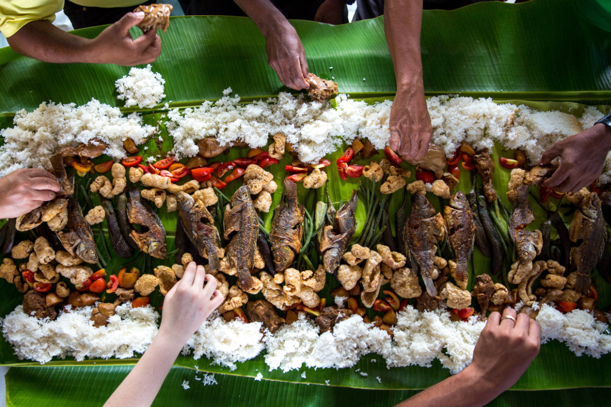 Multiple hands reaching out for food over a Filipino Kamayan feast.