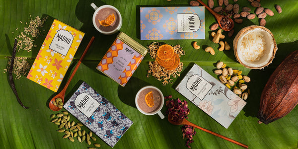 Madhu Chocolate bars and tea laid over banana leaves alongside ingredients used in each product, like cacao, cardamom, vanilla bean, fennel, orange blossom, cashew, coconut, pistachios and more.