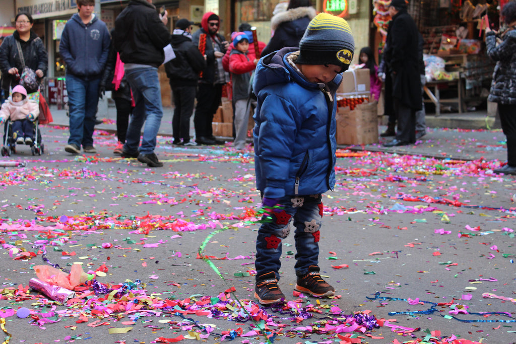 A young child playing with confetti on the streets of Chinatown during a community celebration.