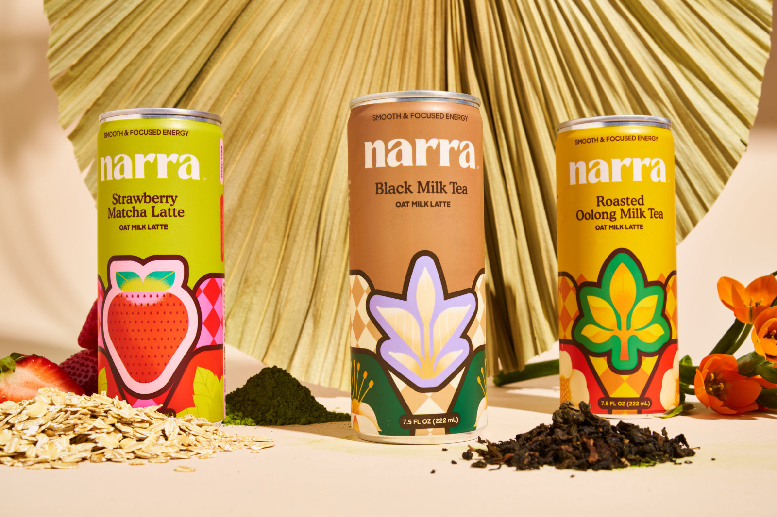 Narra oat milk lattes in Black Milk Tea, Strawberry Matcha Latte, and Roasted Oolong Milk Tea flavors with flowers, matcha, oats, and loose tea placed on a table.
