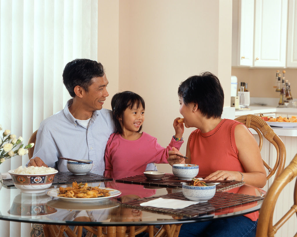 A young Asian family sitting at the dinner table sharing a meal.