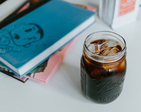 Masadaki kitapların yanında yer alan buzlu yoğun cold brew kahve.