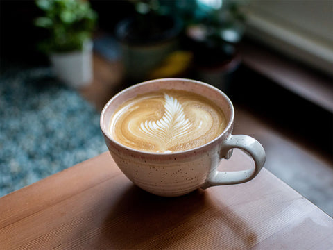 Tezgah üzerinde duran beyaz fincanda latte kahvesi yer almaktad%u0131r.