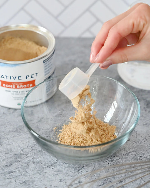 A hand scoops a spoonful of Native Pet Bone Broth Powder into a bowl.