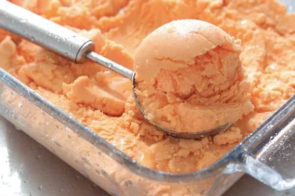 A scoop of cantaloupe sorbet sits atop a glass dish containing the dessert.