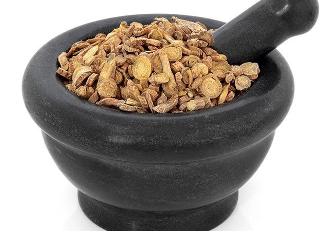 Scutellaria root chinese herbal medicine in a black stone mortar with pestle over white background. Huang qin. Skullcap.
