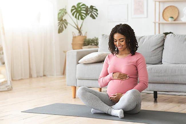 Beautiful happy pregnant african woman hugging her tummy, sitting on sport mat, enjoying her pregnancy, free space