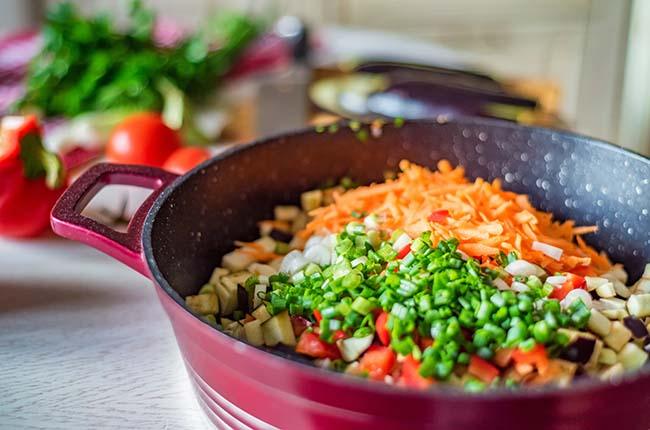 View of fresh chopped organic eggplant, carrot, parsley, tomatoes in pan. Selective focus