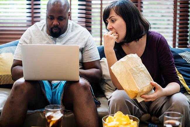 Couple eating junk food and watching tv on the sofa