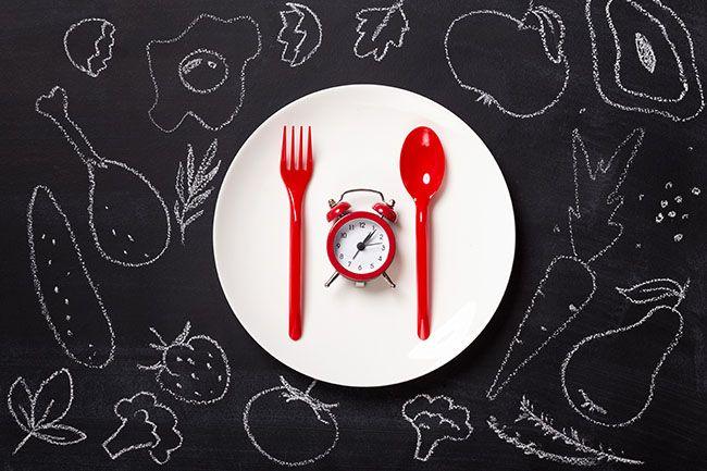 antinutrients matters with timing. Red alarm clock and disposable cutlery on white plate at blackboard with drawn food