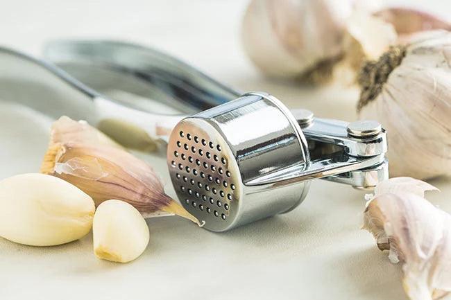 Garlic and garlic press on kitchen table.