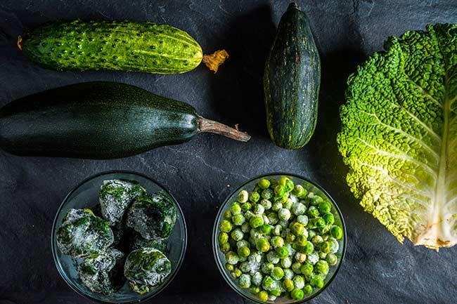 Cucumbers, peas, brussel sprouts, and lettuce on a dark surface