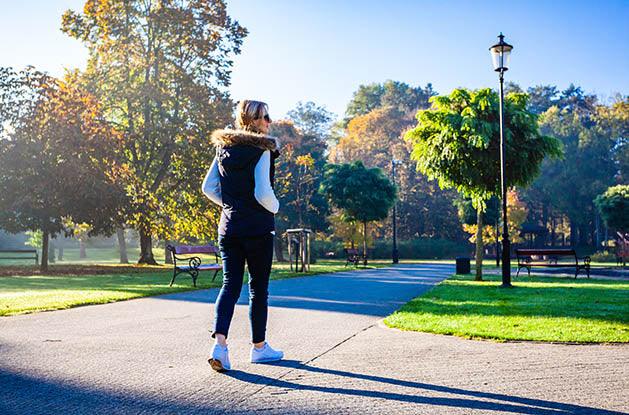 middle aged woman walking in a city park with lots of trees